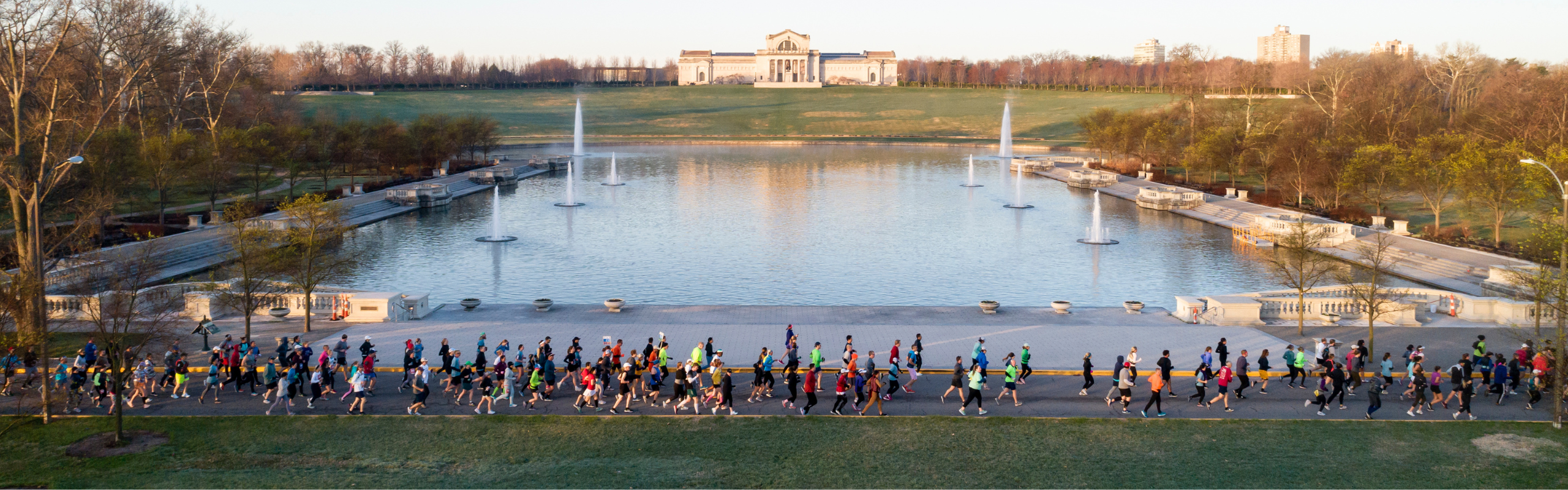 Large group of people running along a lake in the park together. 