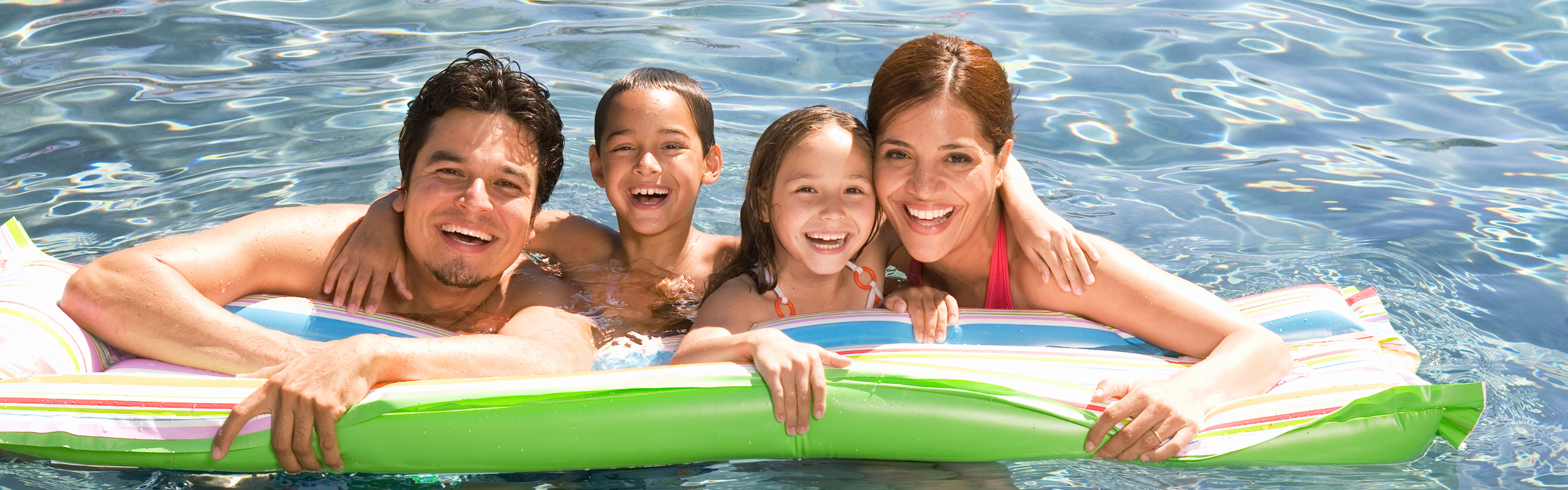 Family smiling together in the pool on a pool float. 