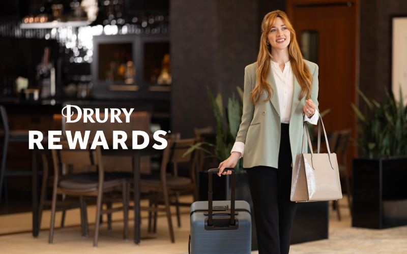 happy business woman with luggage in Drury Hotel lobby promoting the Drury Rewards  program